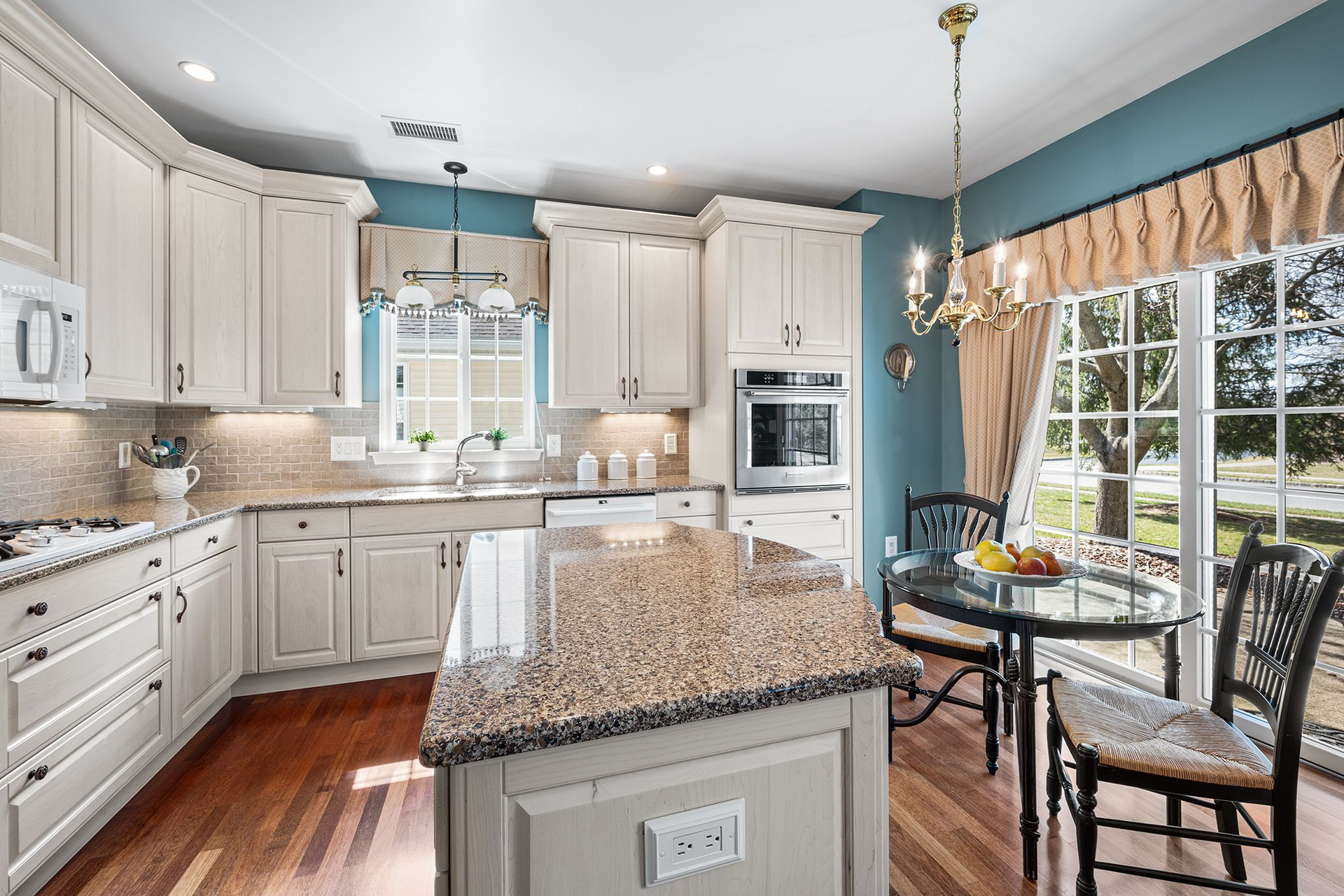 A modern kitchen with cream-colored cabinets, granite countertops, a central island, and a dining area by a sliding door.