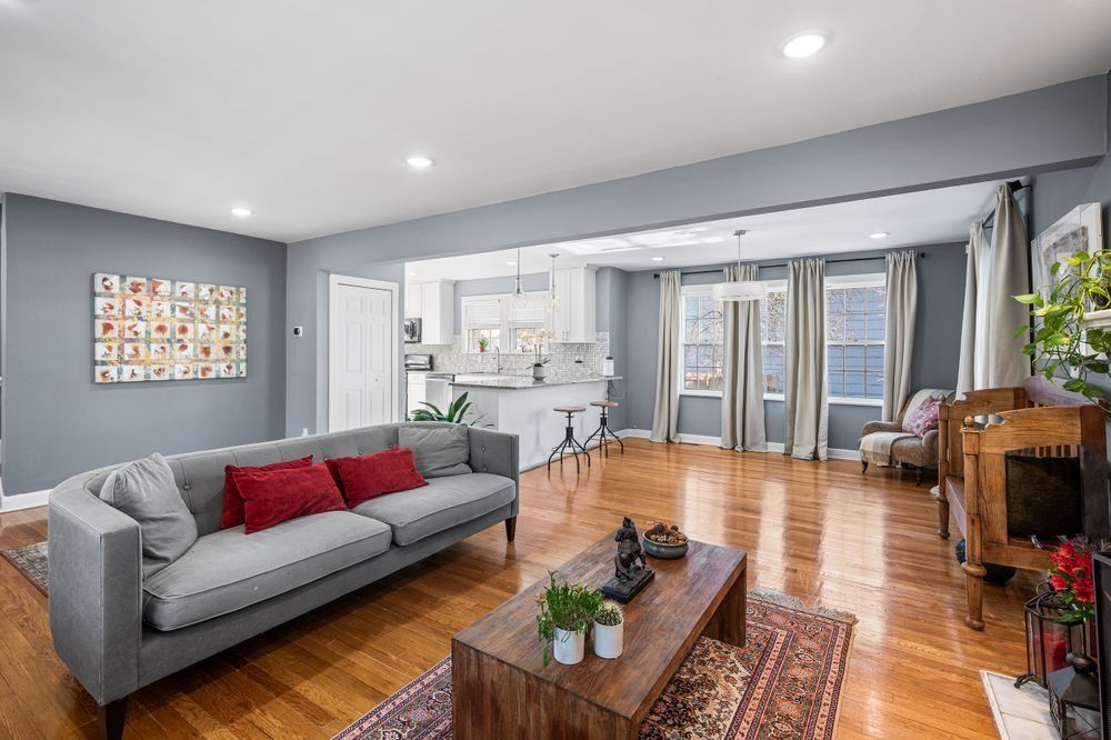 A gray living room with a sofa, wooden coffee table, and area rug, opening into a bright white kitchen with hardwood floors.