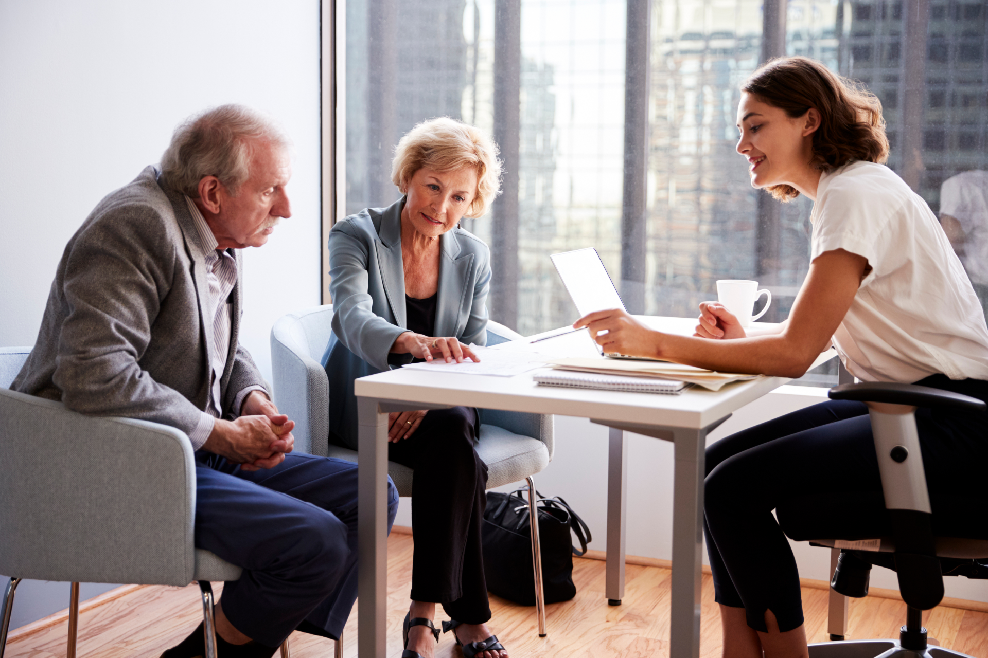 Three people in a bright office meeting around a table, discussing documents