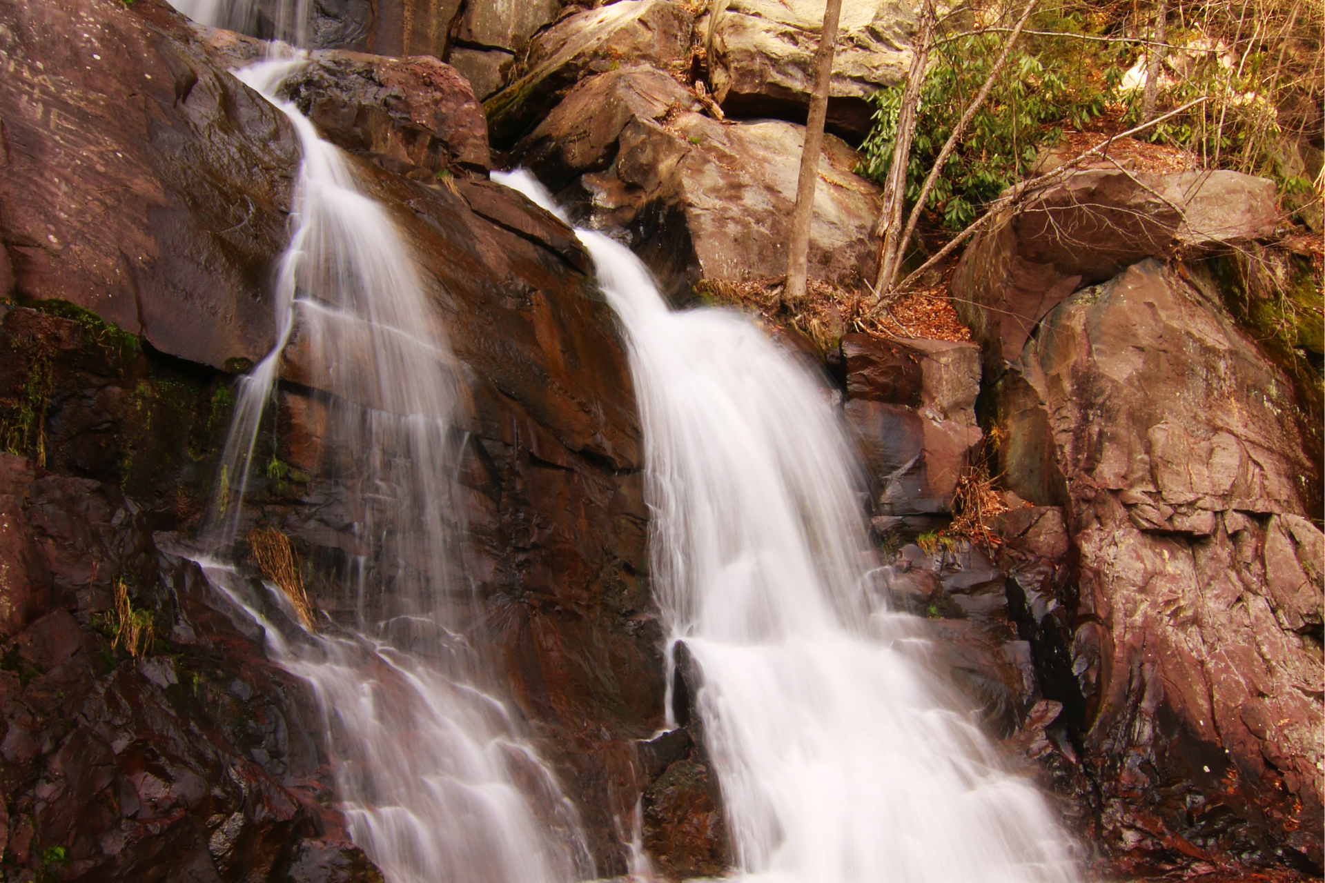 Waterfall cascading over reddish-brown rocks in a forested setting