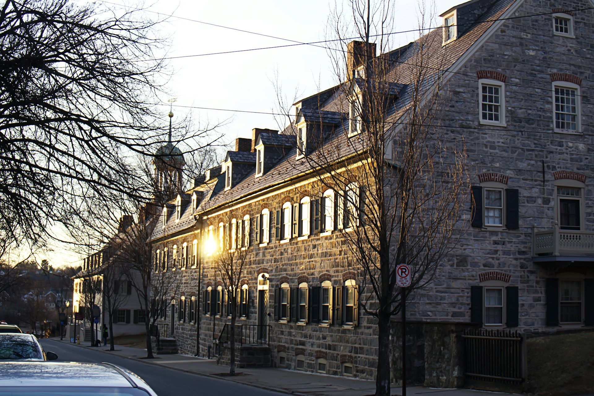Sunlit stone row houses along a quiet street at dusk, with bare trees and parked cars