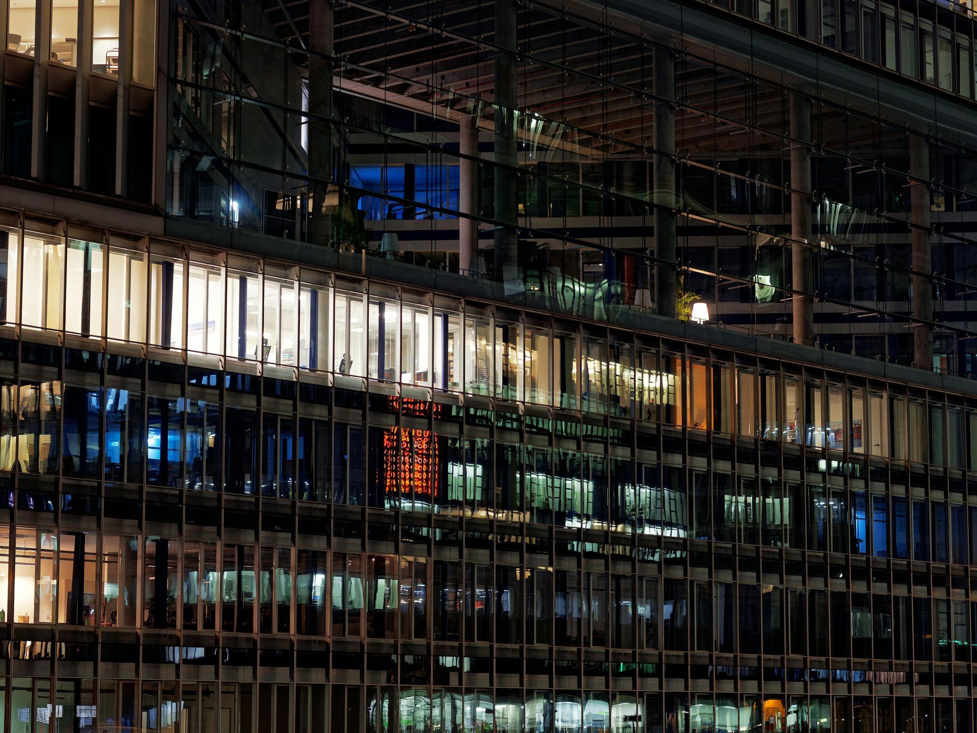 Nighttime view of a modern glass office building with illuminated windows and interior lights