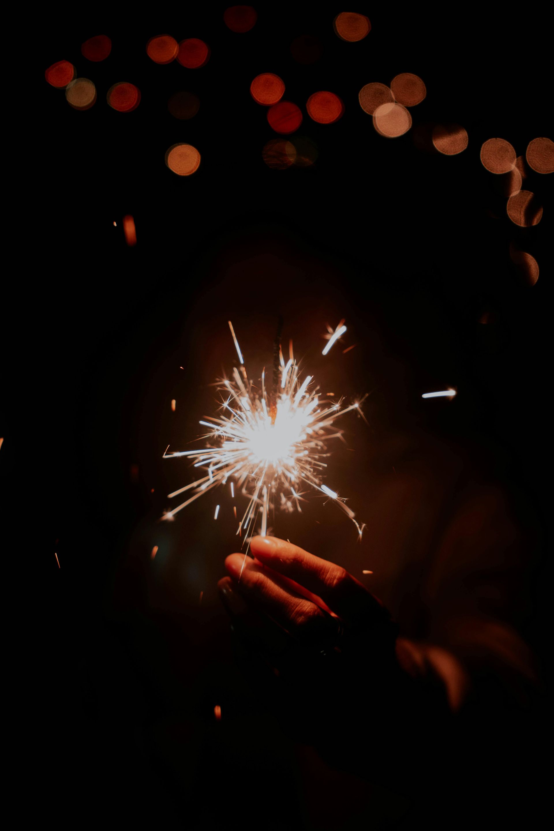 Hand holding a bright sparkler in the dark with warm bokeh lights in the background