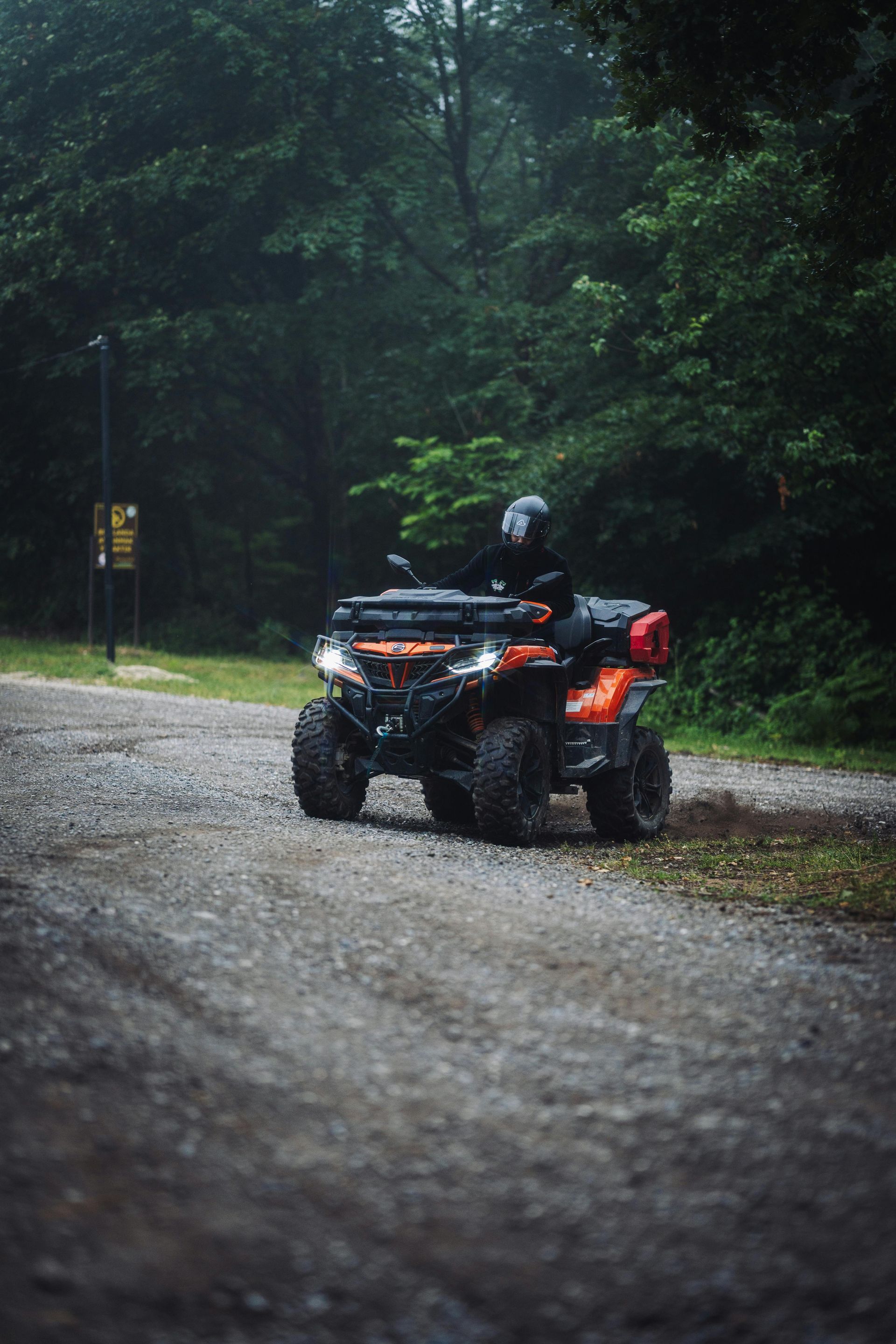 ATV with rider on a wet gravel road in a dark, rainy forest