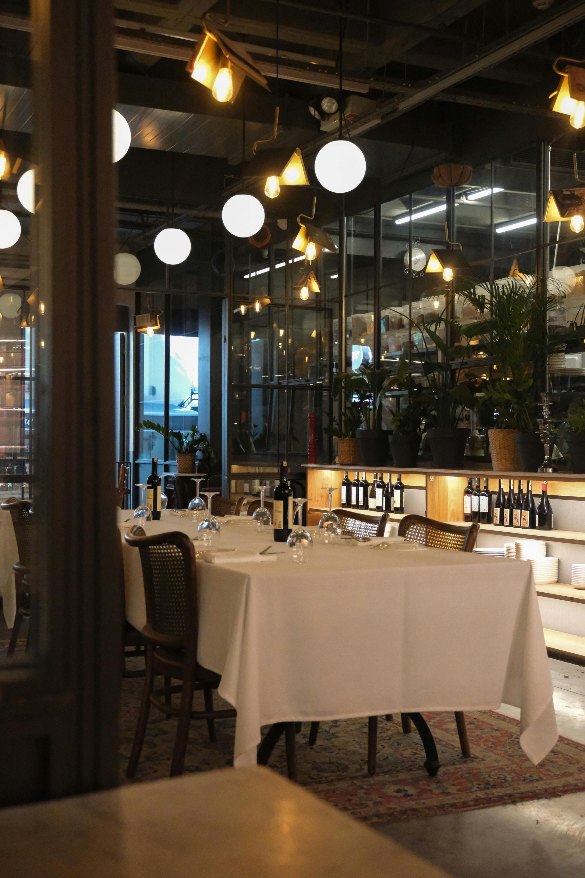 Elegant restaurant interior with white tablecloths, warm pendant lights, and glass walls at night
