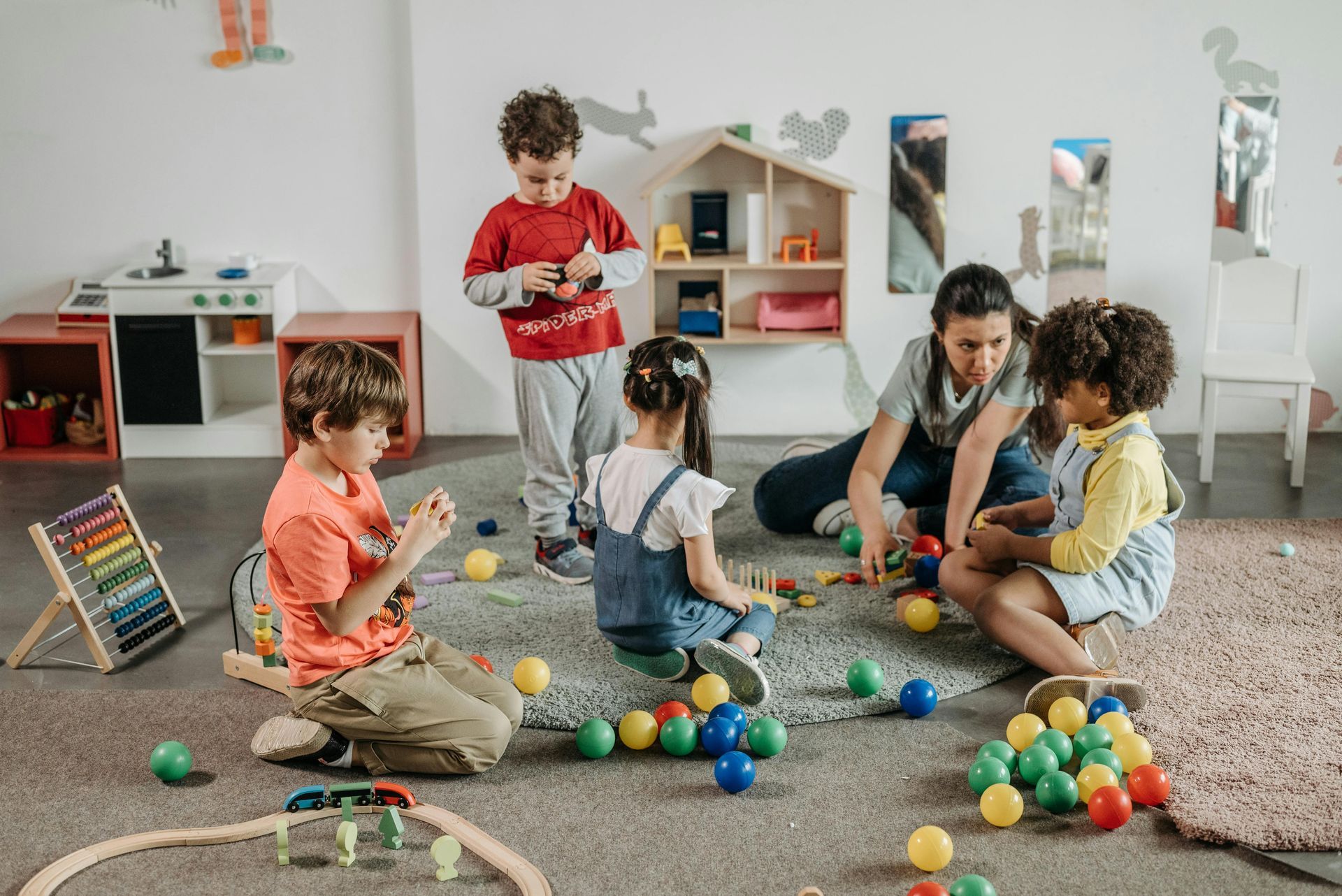 Children playing with colorful balls while a caregiver sits nearby in a bright classroom