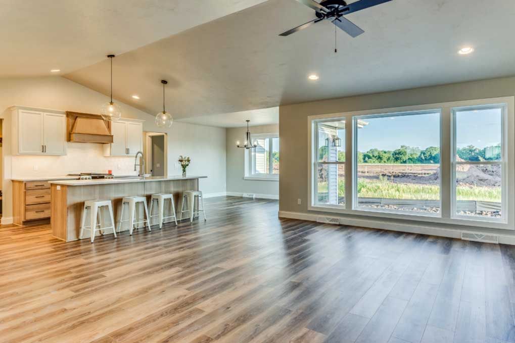Bright open-concept kitchen and living area with island, wood floors, and large windows overlooking a field