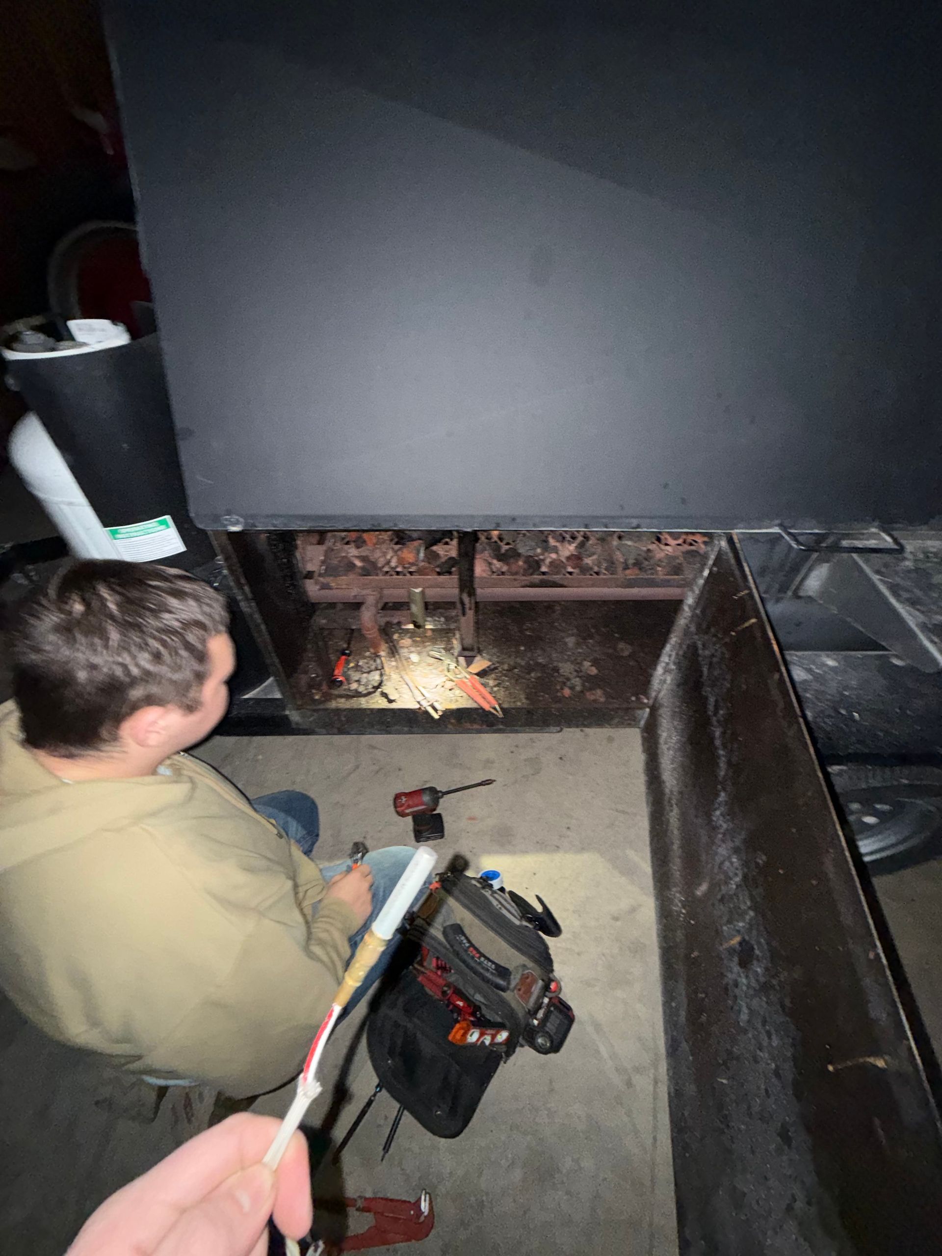 A person holds a white wire while another person works inside the open bottom panel of a large, black metal unit.