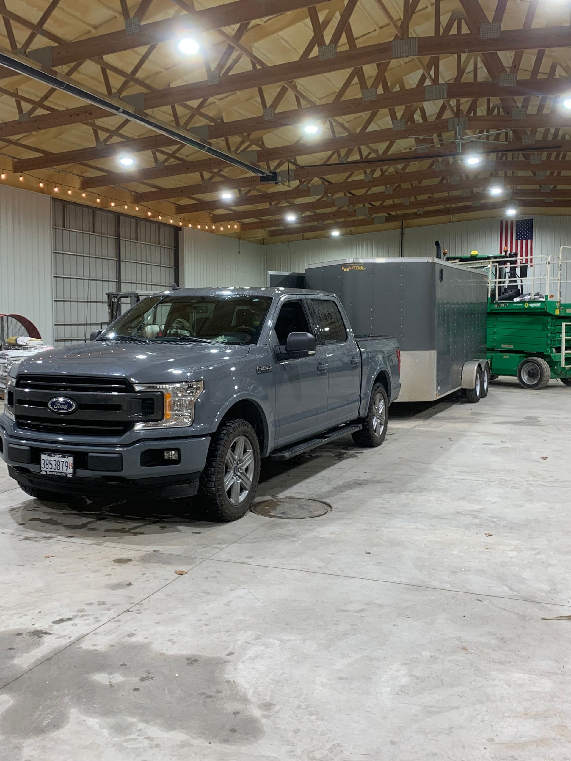A gray Ford pickup truck hitched to an enclosed cargo trailer parked inside a large, well-lit storage building.