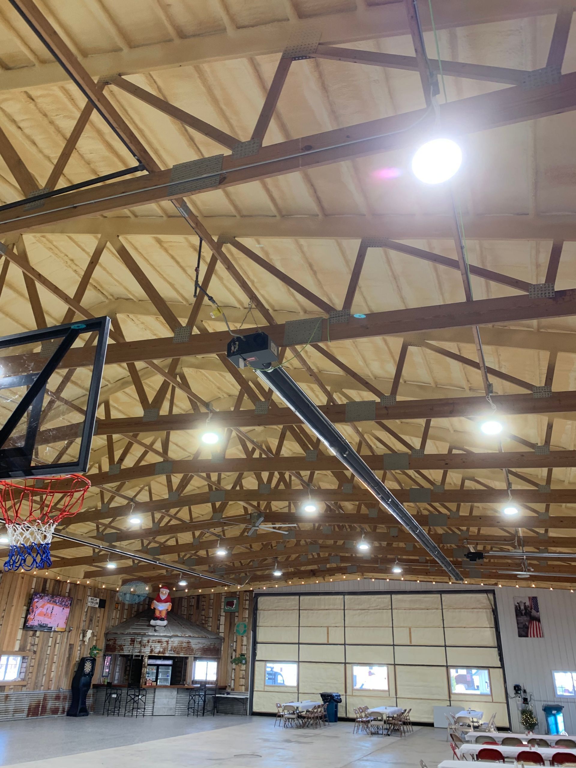 Interior view of a rustic, high-ceilinged recreational hall with wood trusses, multiple light fixtures, and a gym area.