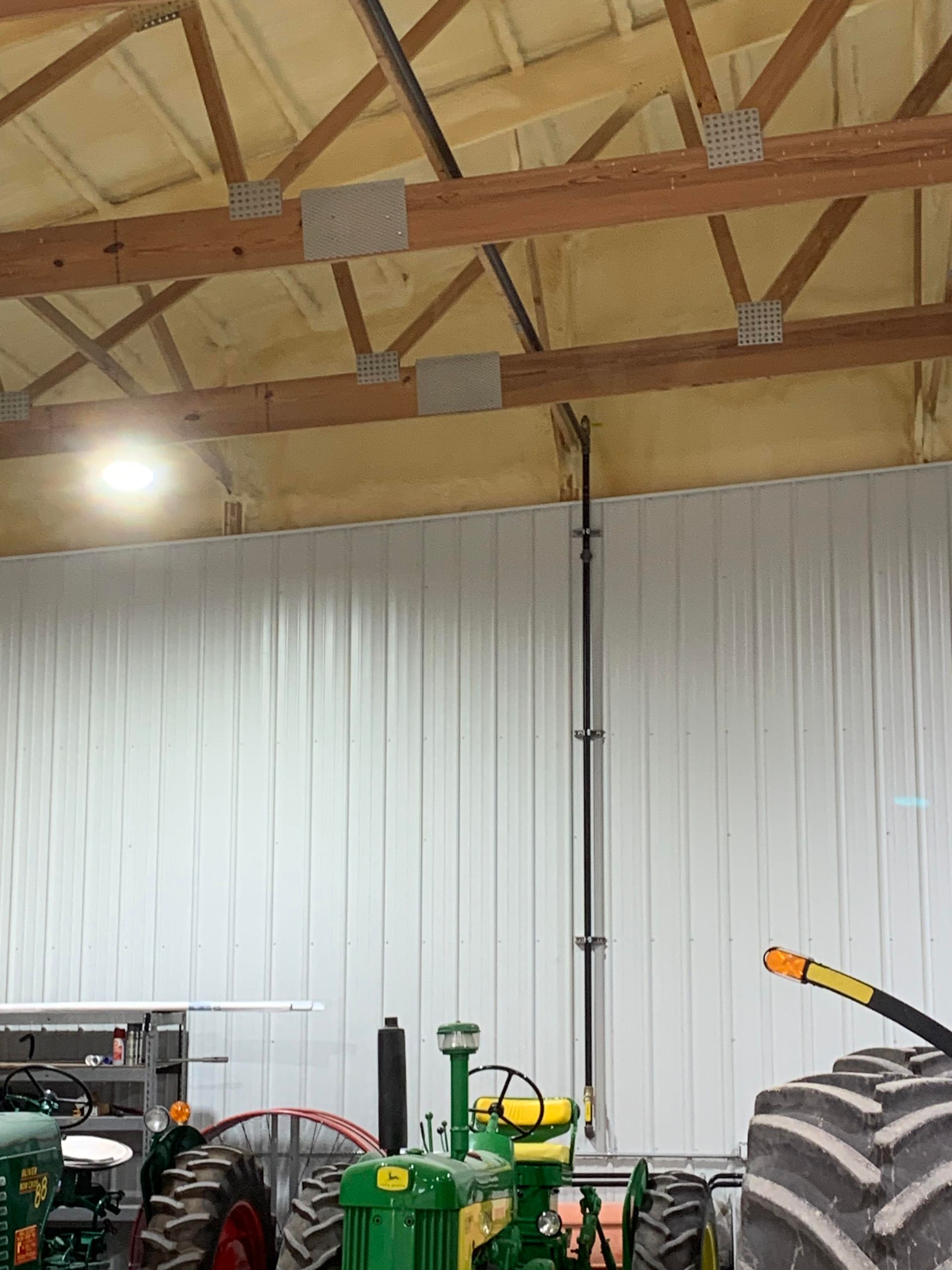 Two green vintage tractors parked inside a modern barn with light-colored metal walls and wooden roof trusses.