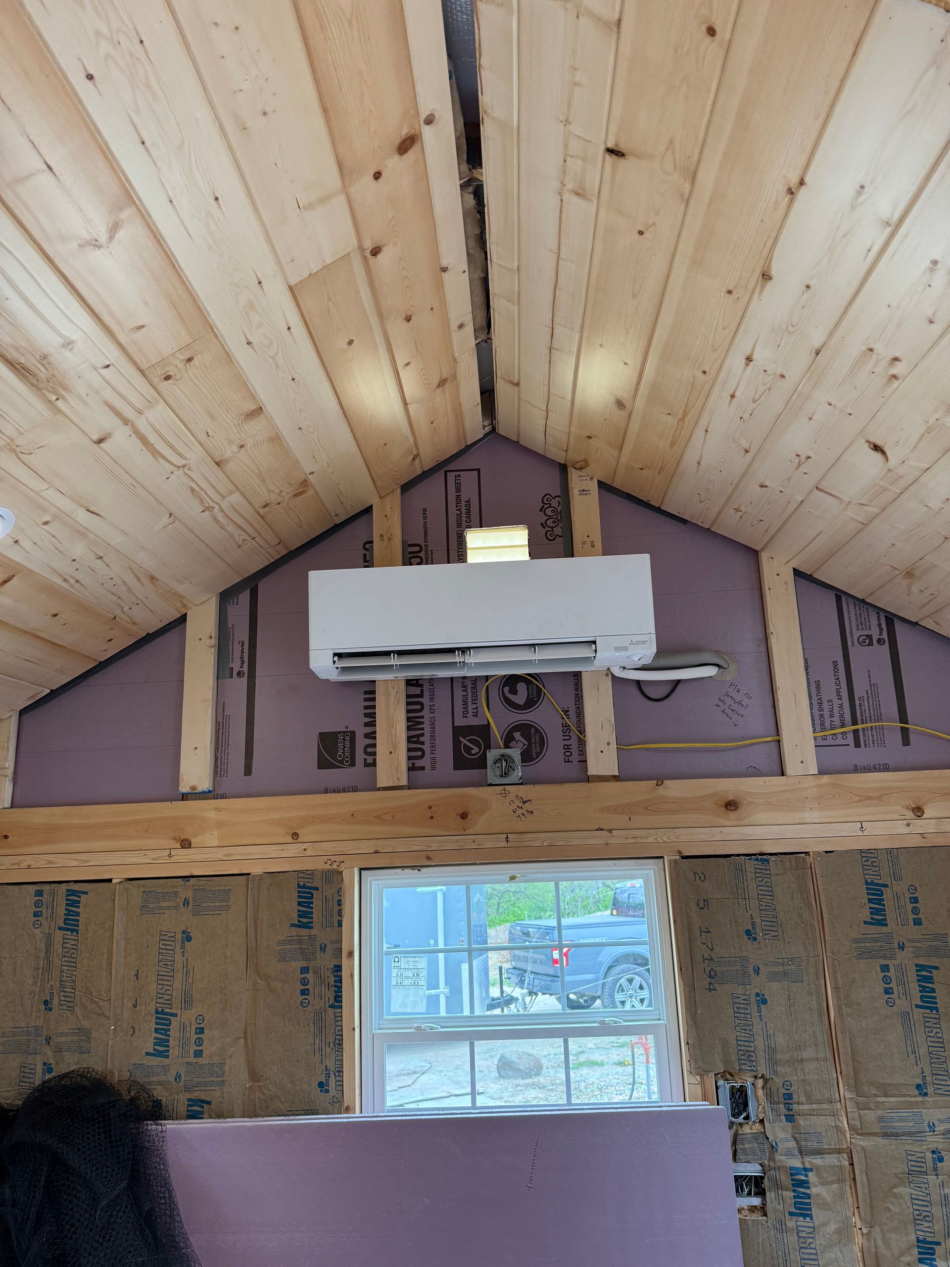 A wall-mounted ductless mini-split air conditioner installed on a partially finished wall with wood ceiling paneling.