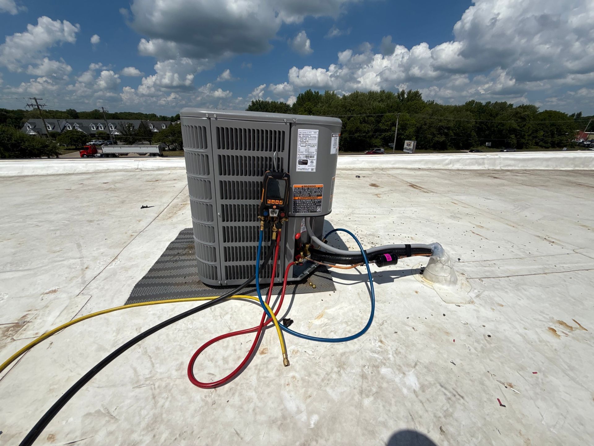 An air conditioning unit on a flat white roof with technician gauges connected to its service ports.