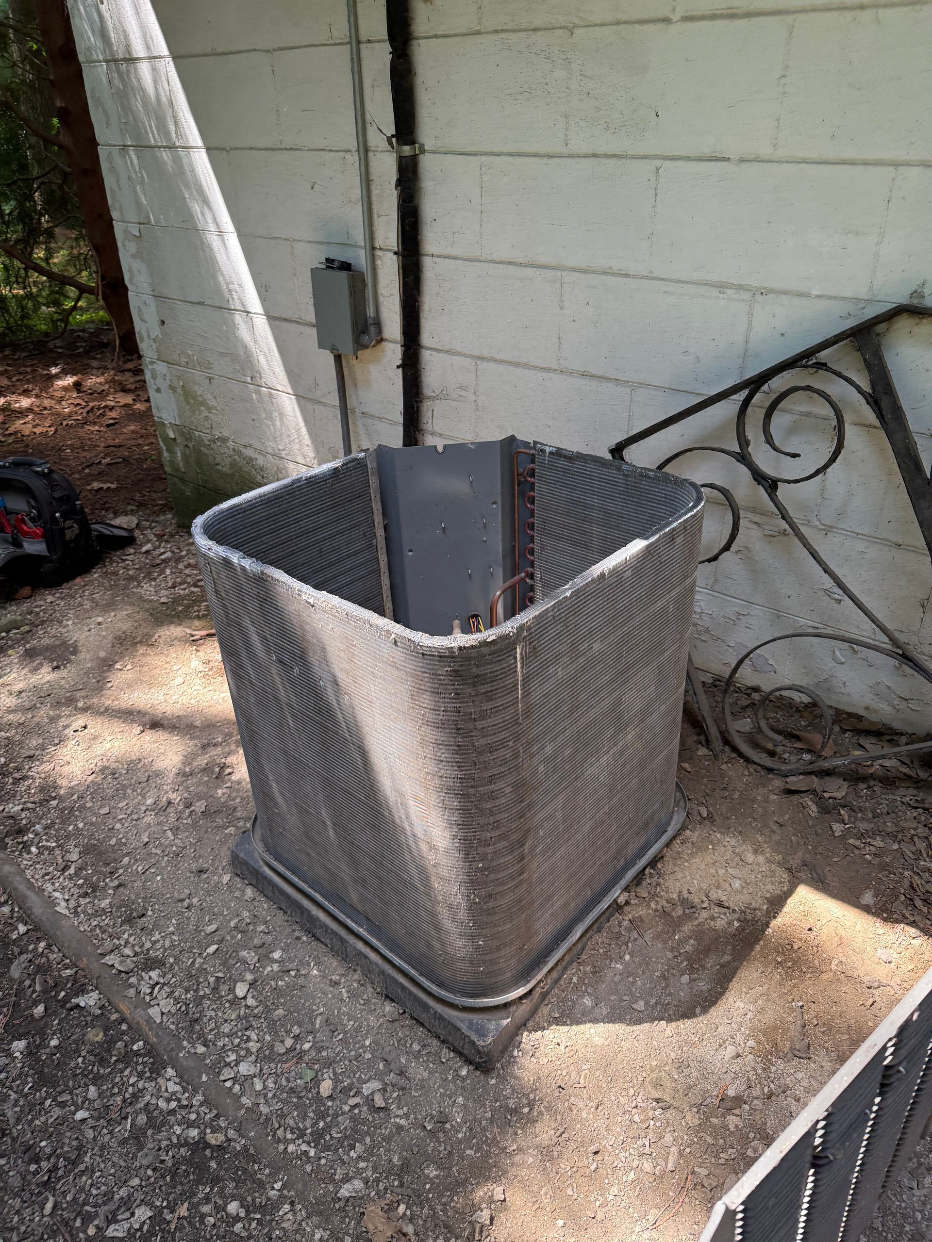 A square HVAC condenser coil unit sits exposed outdoors against a white cinder block wall.