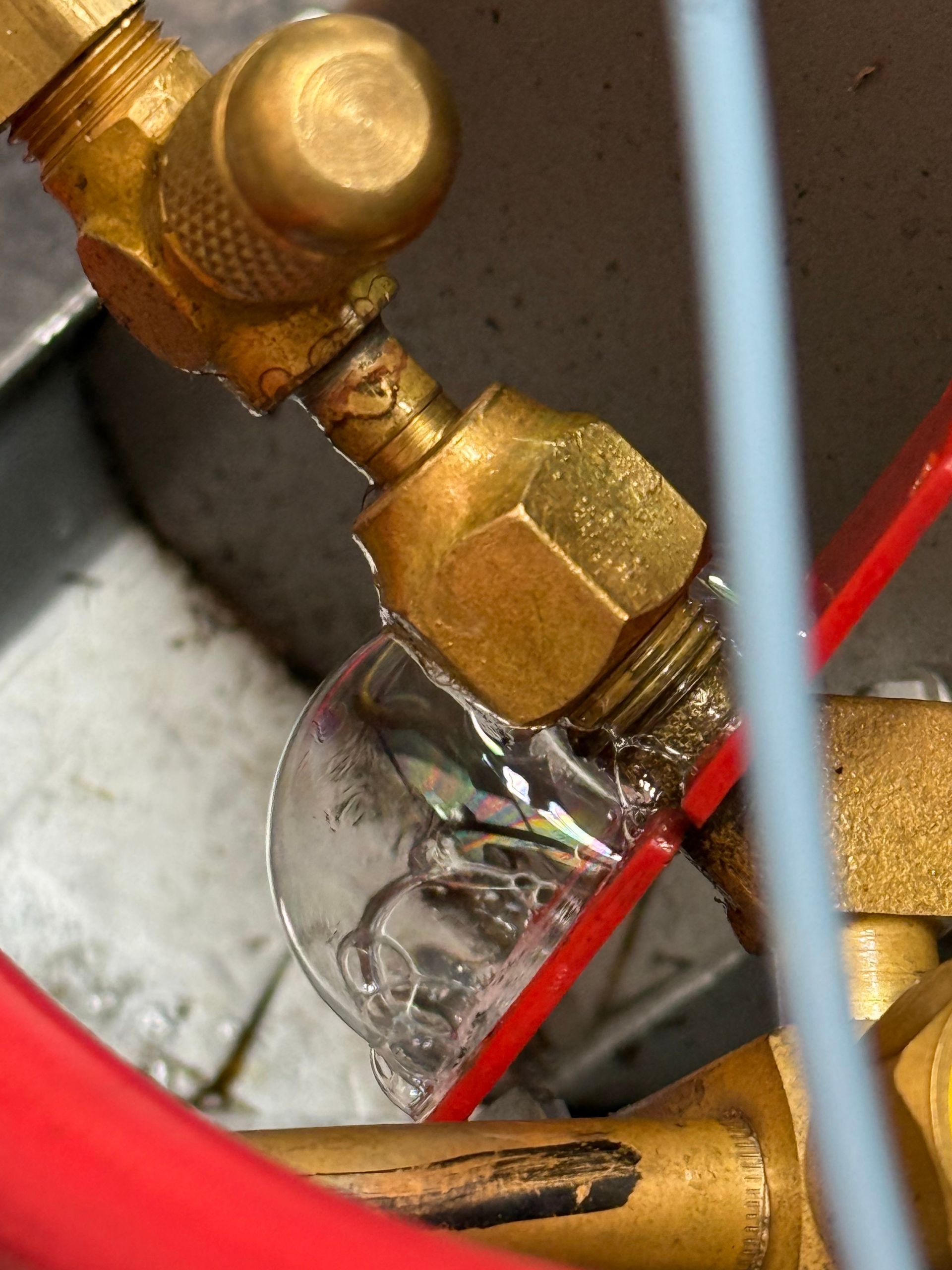 A close-up of a brass refrigerant valve fitting showing a bubbling leak detection solution indicating a gas leak.