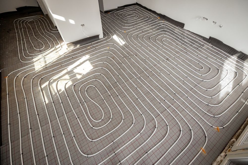 White plastic tubing laid in a serpentine pattern on a gray grid floor for a radiant floor heating system installation.