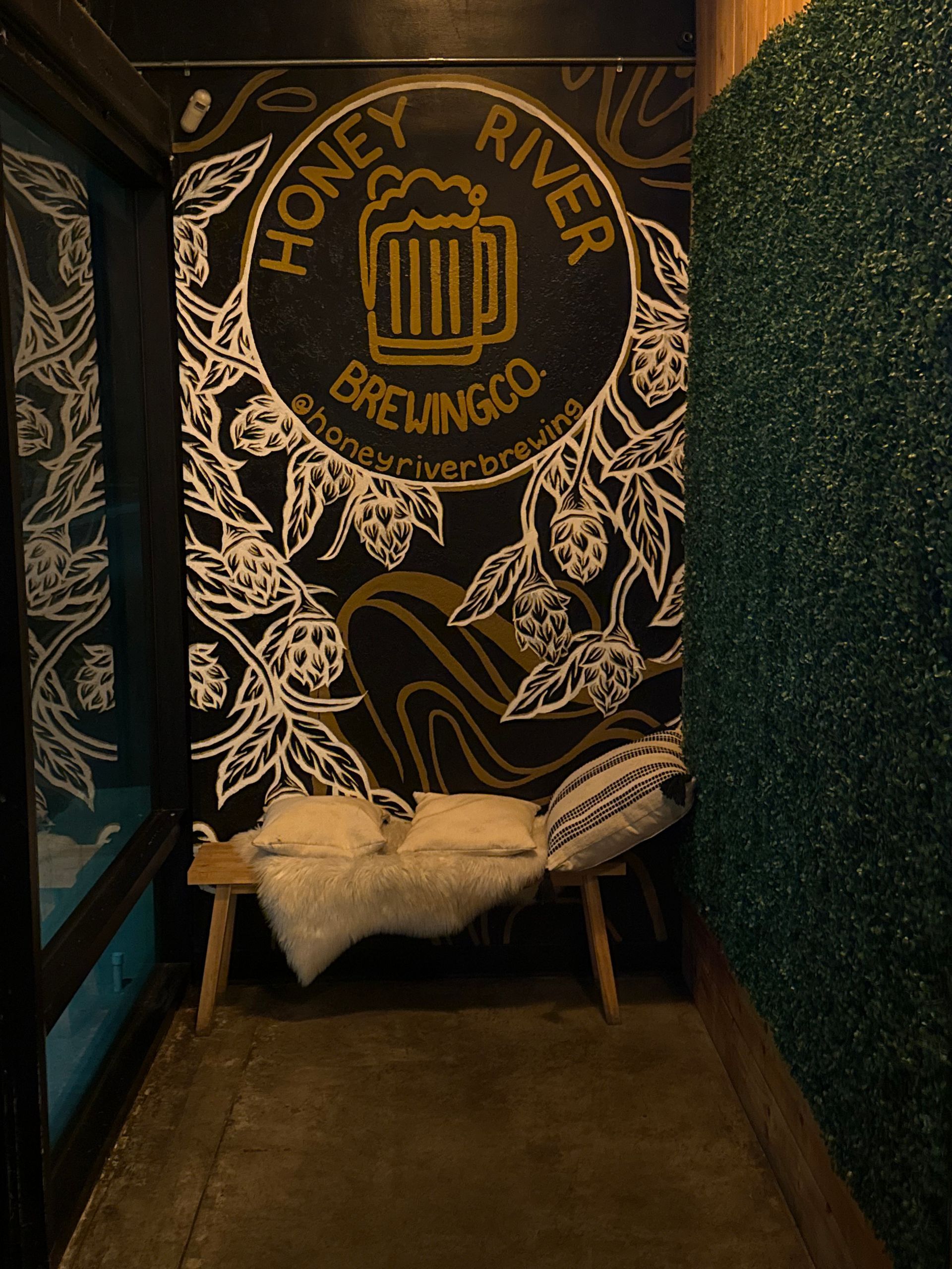 A Honey River Brewing Co. mural with a bench and pillows, in a dimly lit, cozy space.