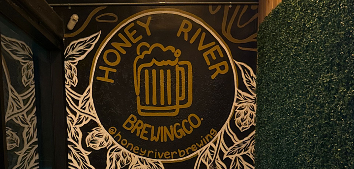 Honey River Brewing Co. mural on a black wall with a bench and pillows, beside a green wall, in a narrow space.