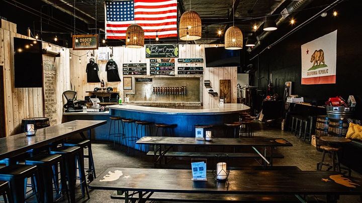 Interior of a bar with an American flag, beer taps, tables, and a California flag.