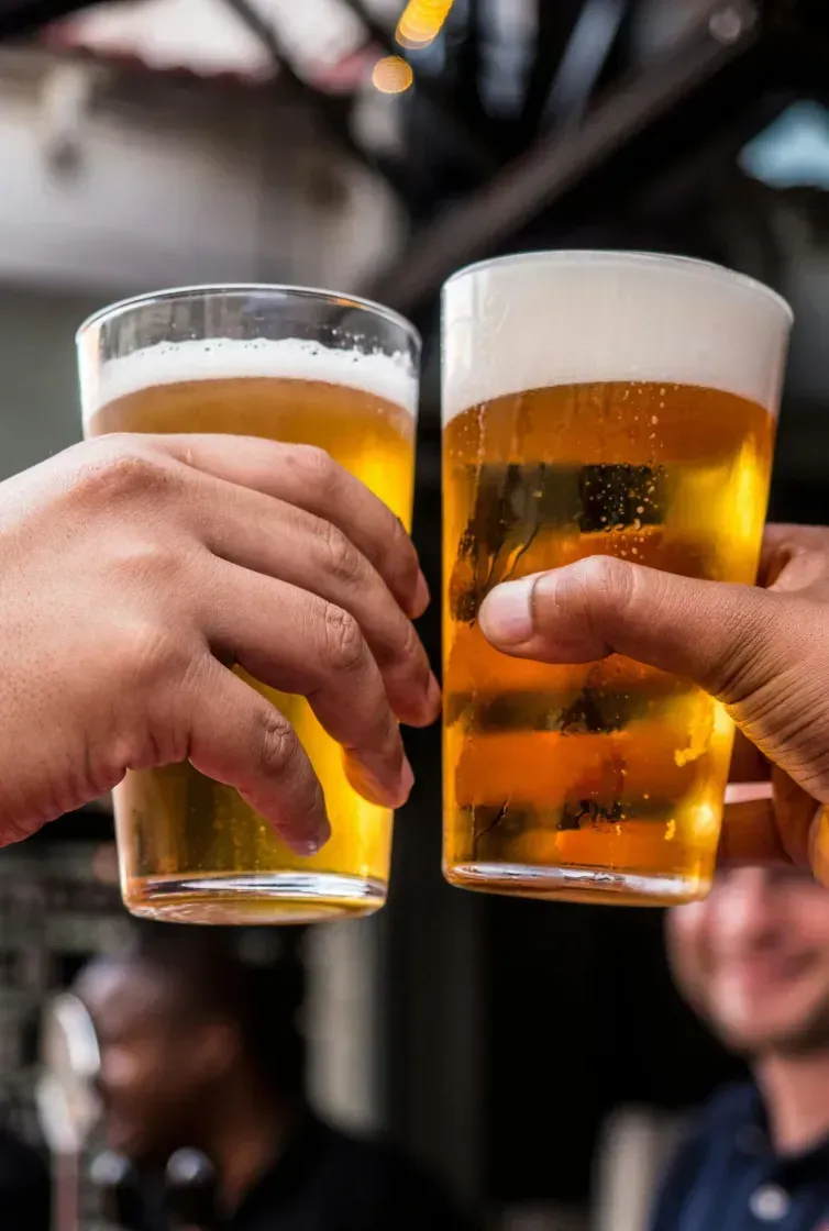 Two hands holding glasses of beer clinking together in celebration.