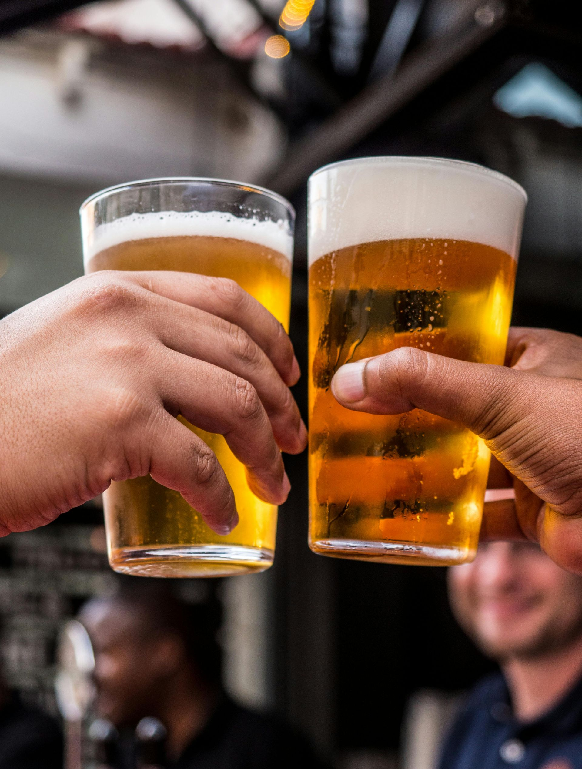 Two hands holding glasses of beer clinking together in celebration.