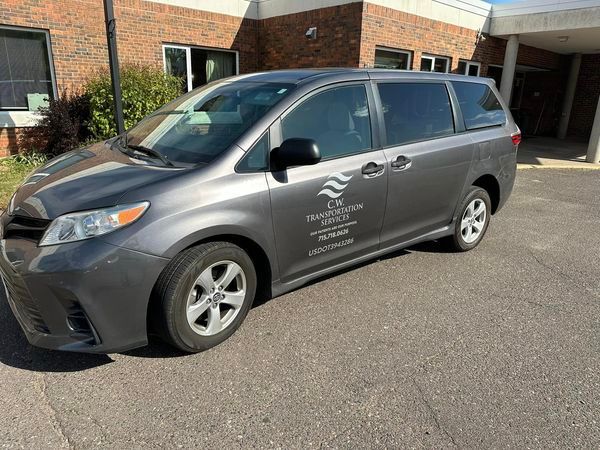 A gray minivan is parked in front of a brick building.