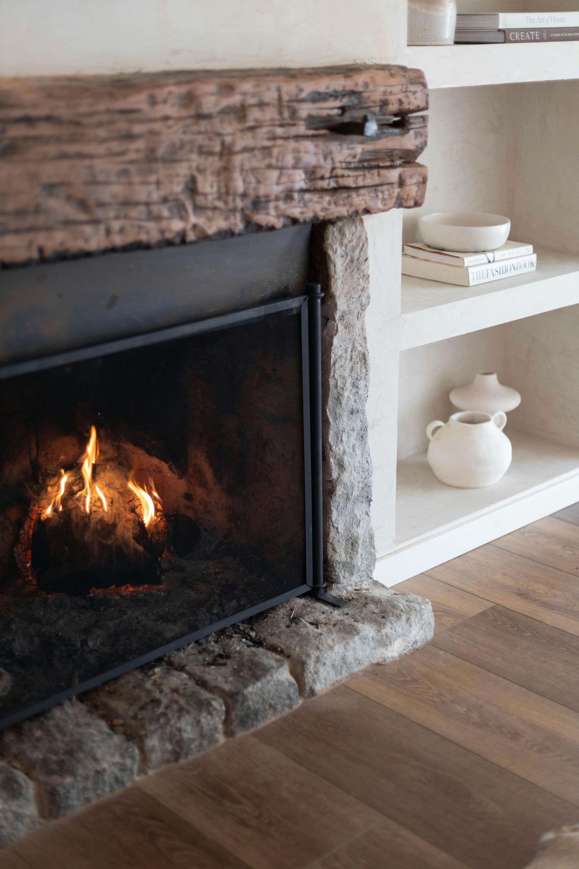 Fireplace with lit fire, stone surround, wooden mantel, and built-in white shelves with decor.