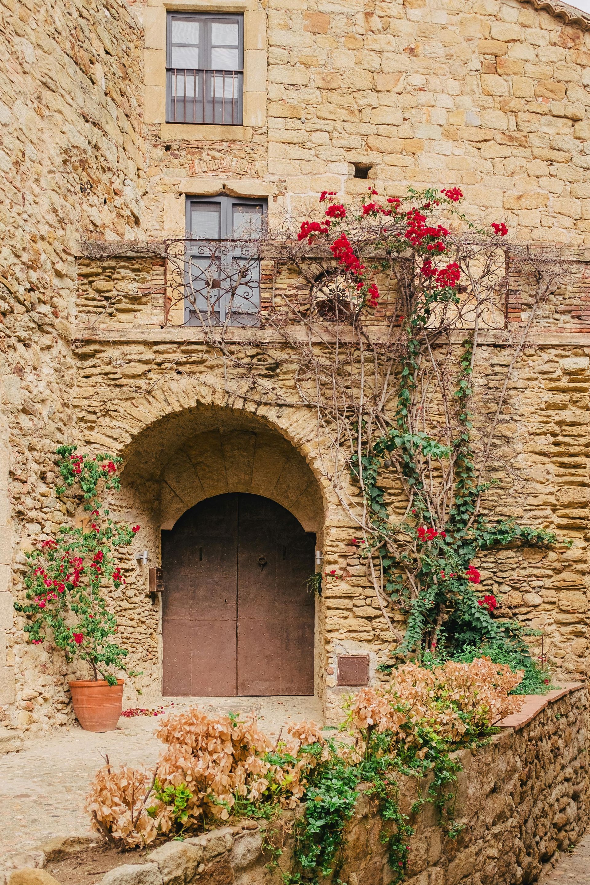 Stone building with arched entrance and red flowering vines.