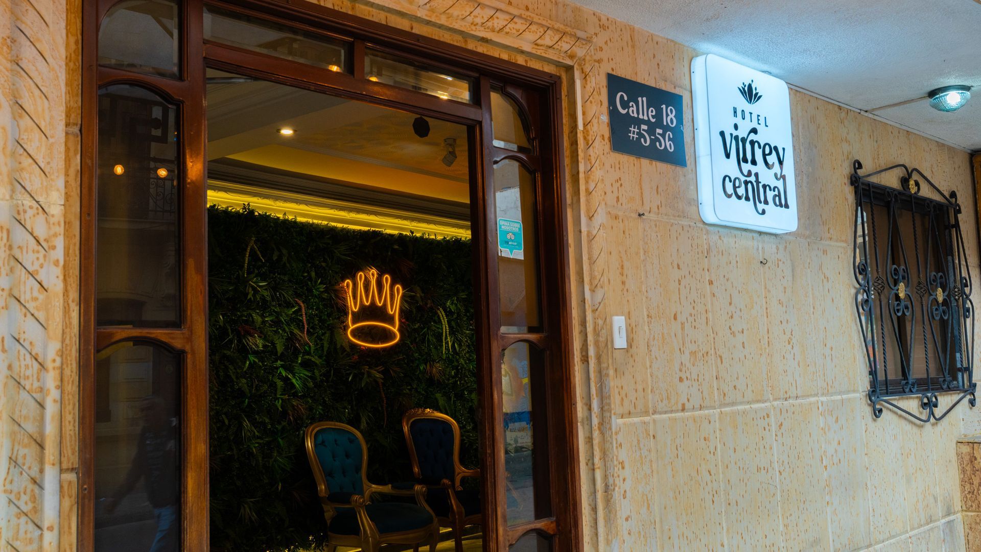 Entrada de Hotel Virrey Central en Bogotá, acceso con letrero del hotel y señal de Calle 18, lobby iluminado con pared verde y neón en forma de corona.