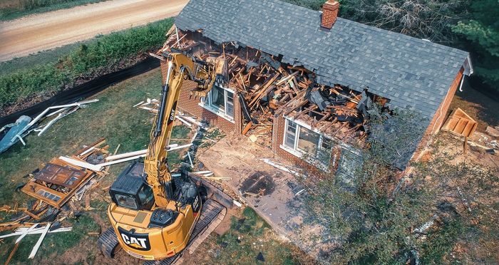 An aerial view of a house being demolished by a bulldozer.