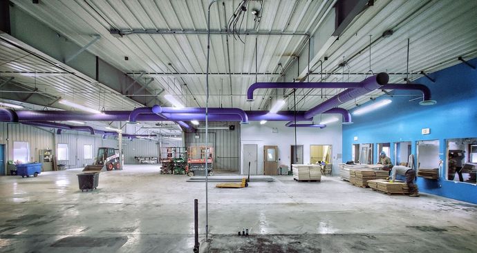 A large empty warehouse with purple pipes hanging from the ceiling.