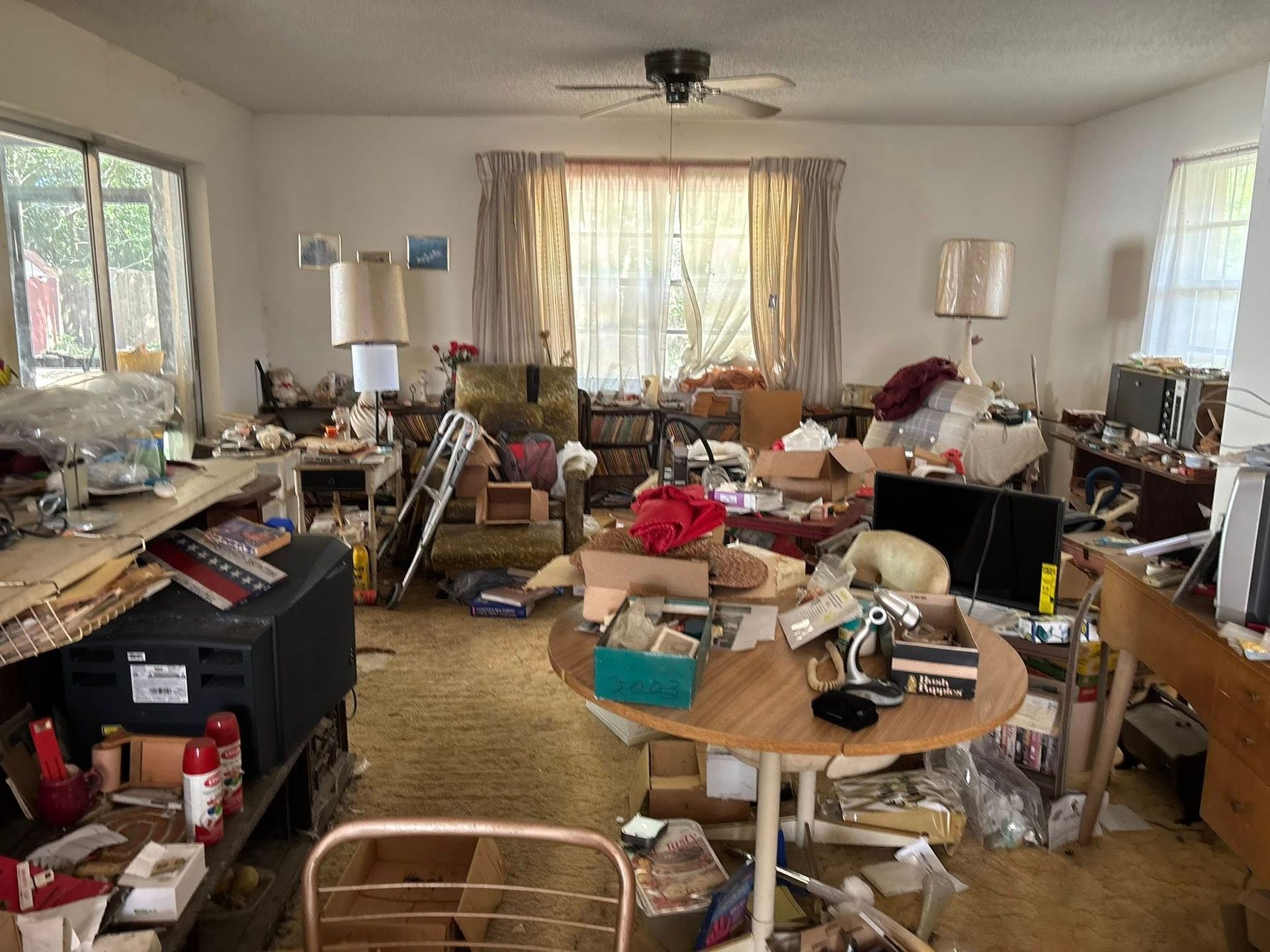 Cluttered living room: furniture, boxes, and items scattered on the floor and surfaces. 