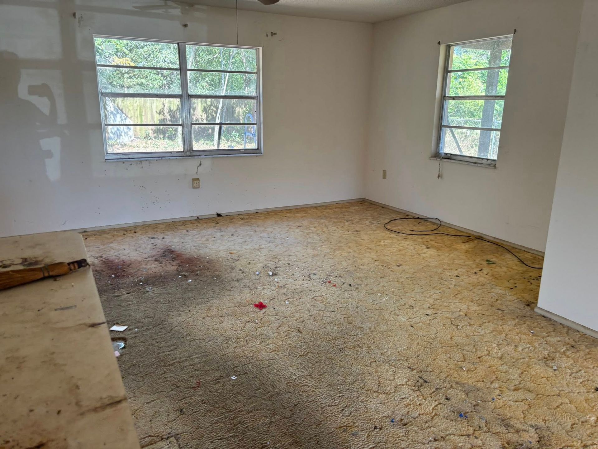 Empty room with two windows, bare walls, and debris-covered floor.