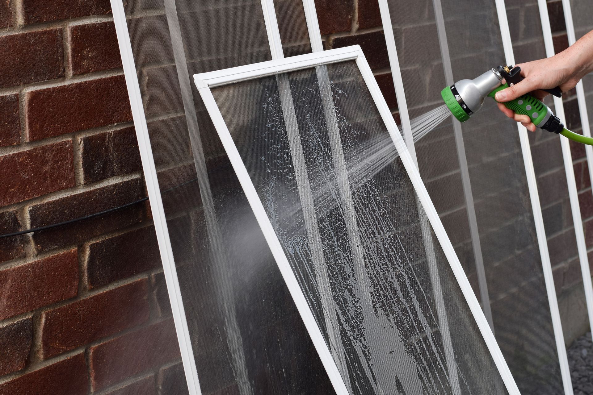 Person spraying water on window screens with a hose outside a brick building.