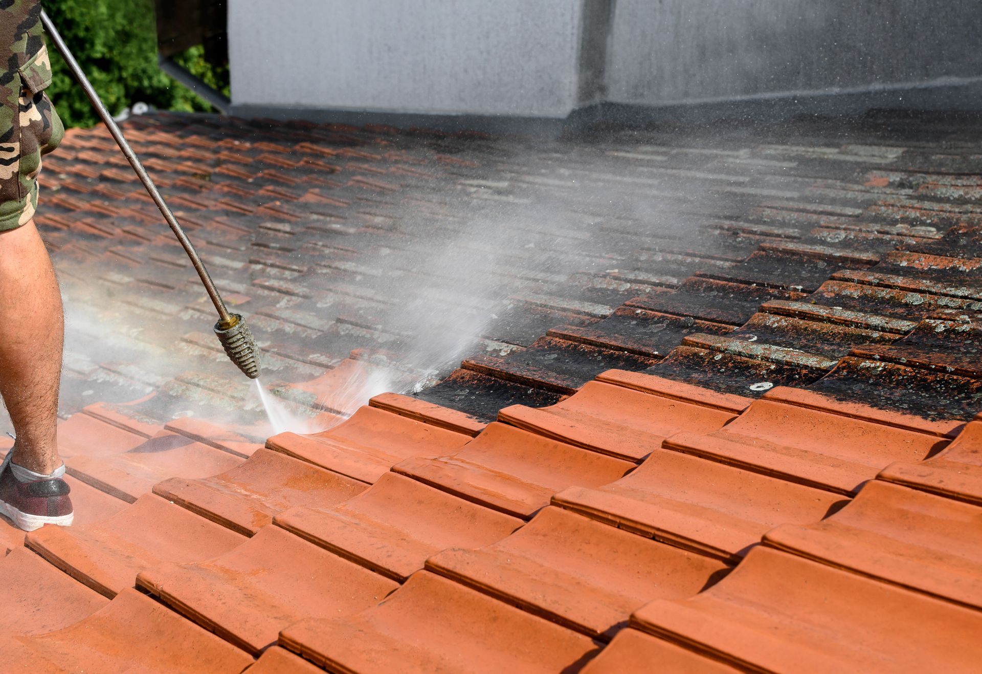 Man power washing a red tile roof, removing dirt and moss.