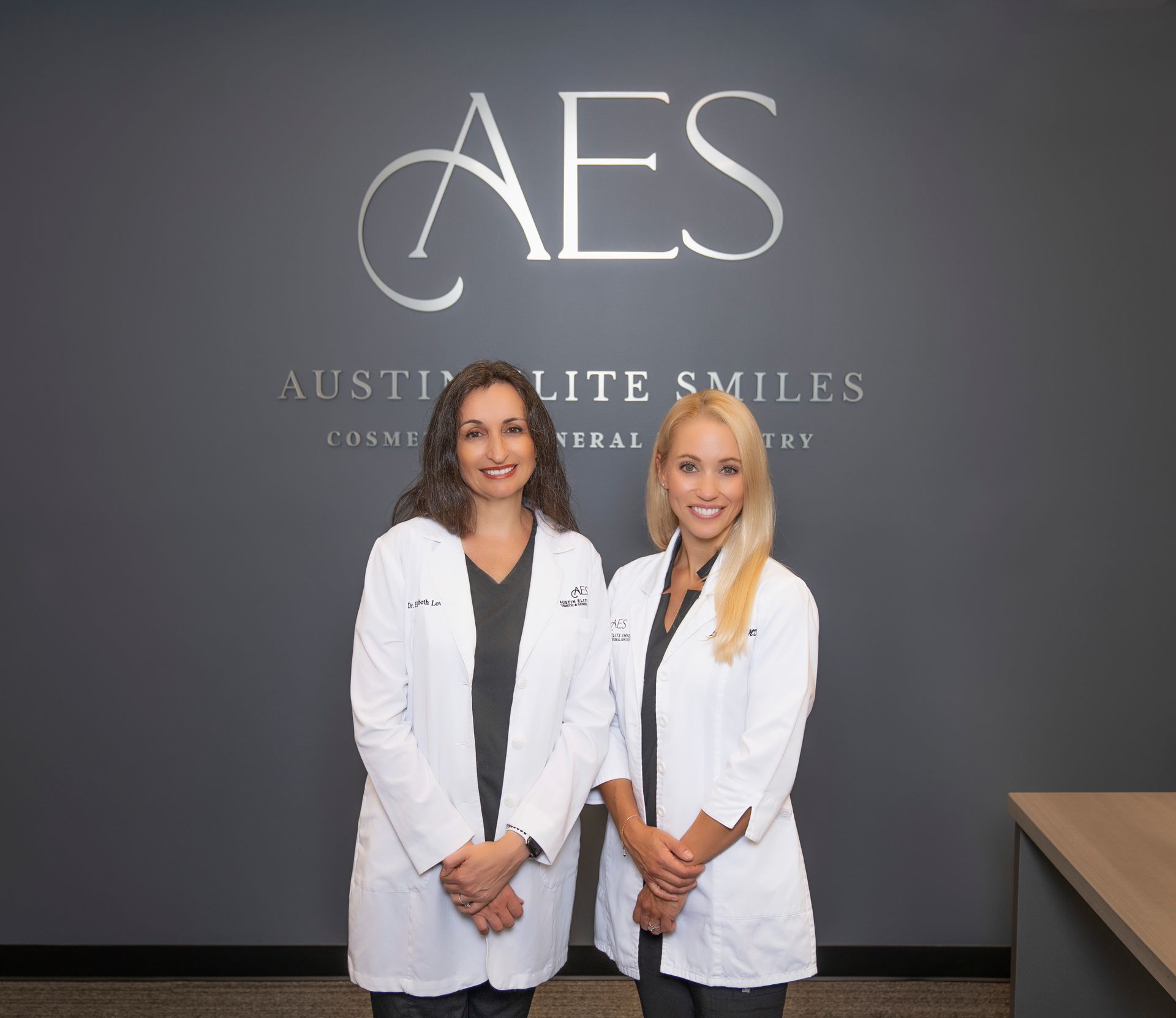 Two women dentists standing in front of office wall.