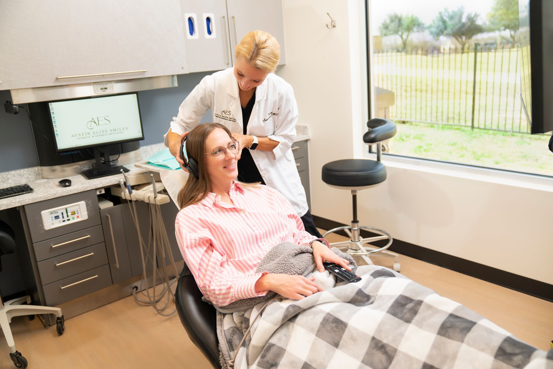 Dentist examining a patient in a dental chair beside a window.