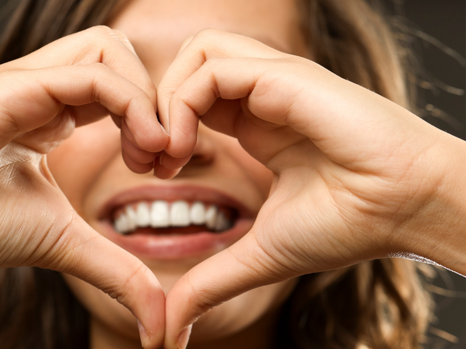 Woman smiling, forming heart shape with hands over her mouth.