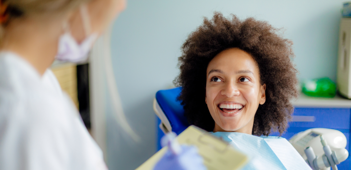 A smiling patient in a dentist's chair is attended to by a dentist in a dental office.