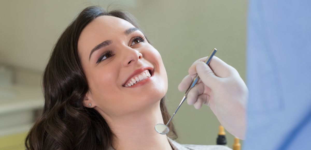 Woman smiling during dental checkup as a dentist examines her teeth with a mirror.