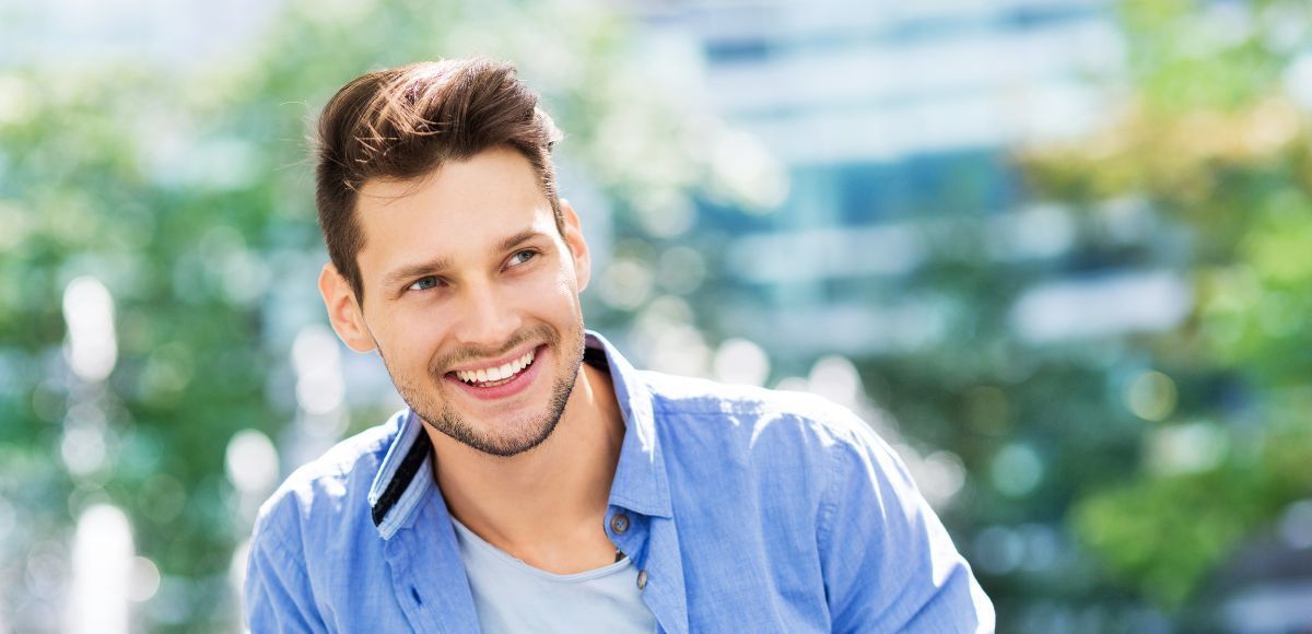 Smiling man in a blue shirt outdoors with a blurred green background
