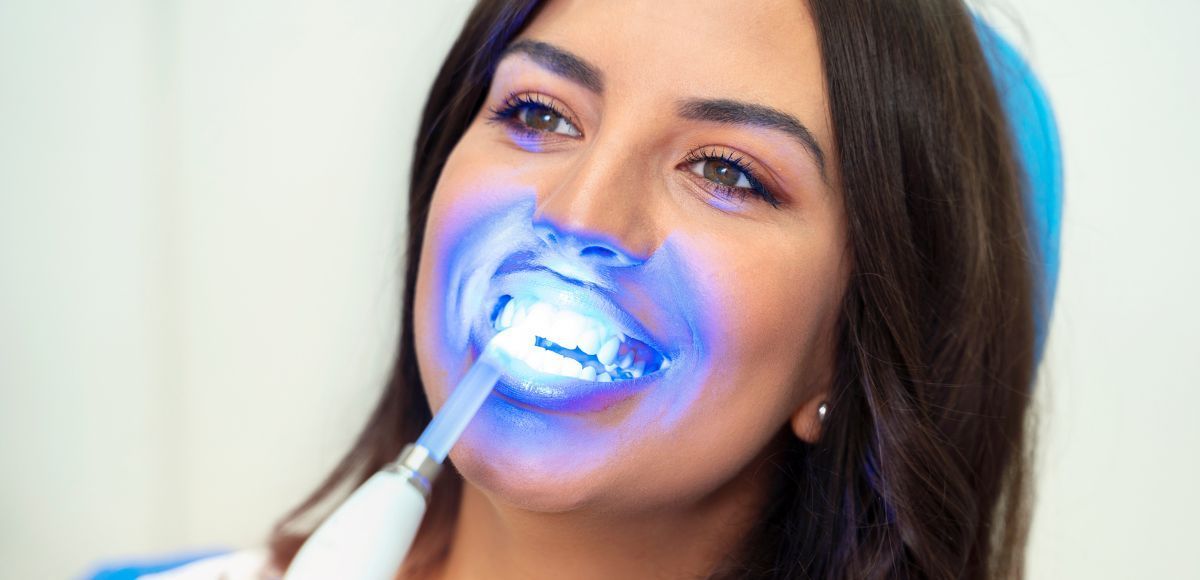 Woman receiving blue-lit dental treatment with a teeth-whitening wand