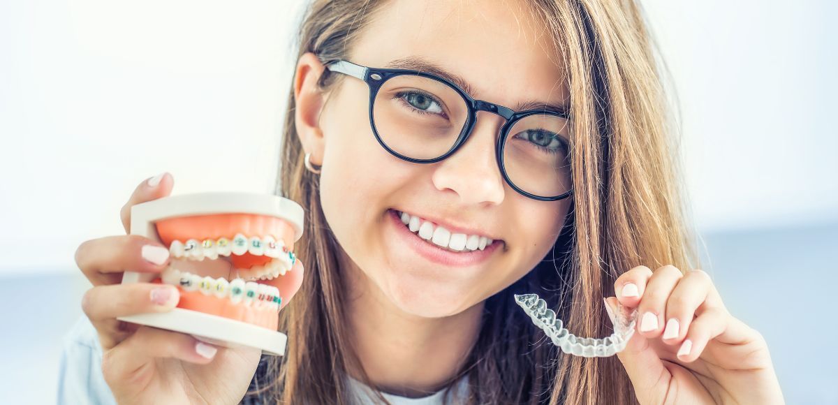 Smiling person holding dental braces model and clear aligner against a bright background