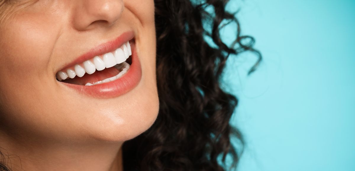 Close-up of a smiling person with red lipstick against a light blue background