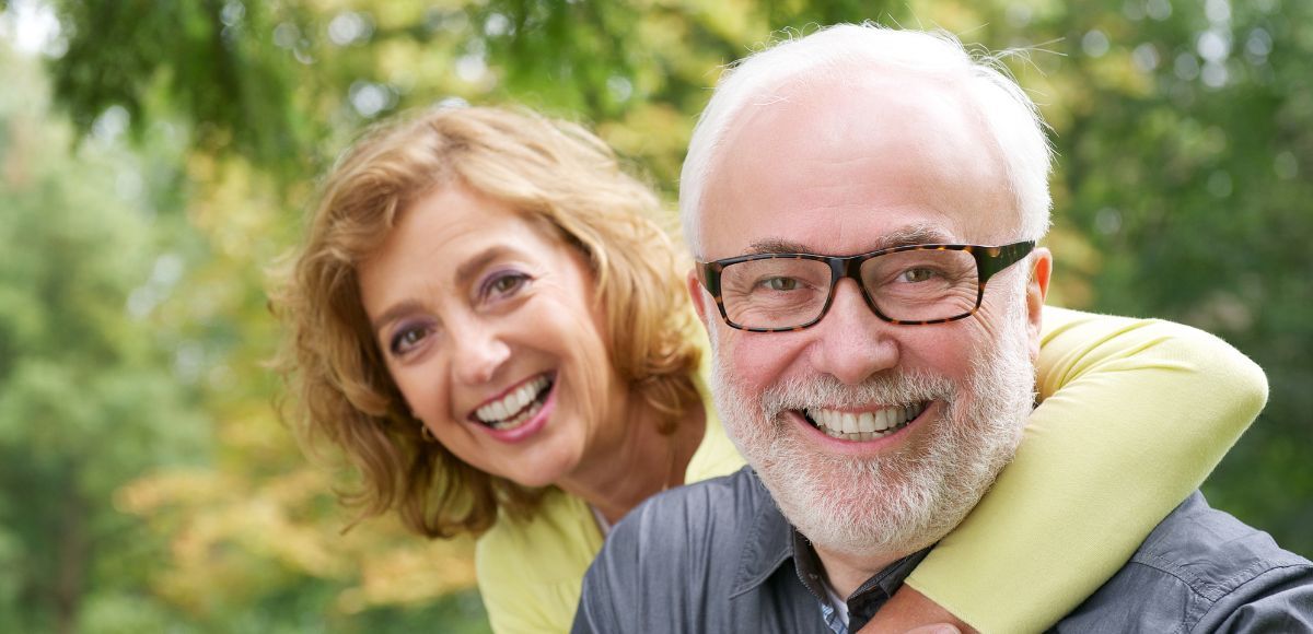 Smiling couple outdoors in a park, with the woman leaning on the man's shoulder.