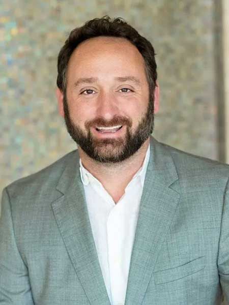 A man with a beard is wearing a suit and smiling.