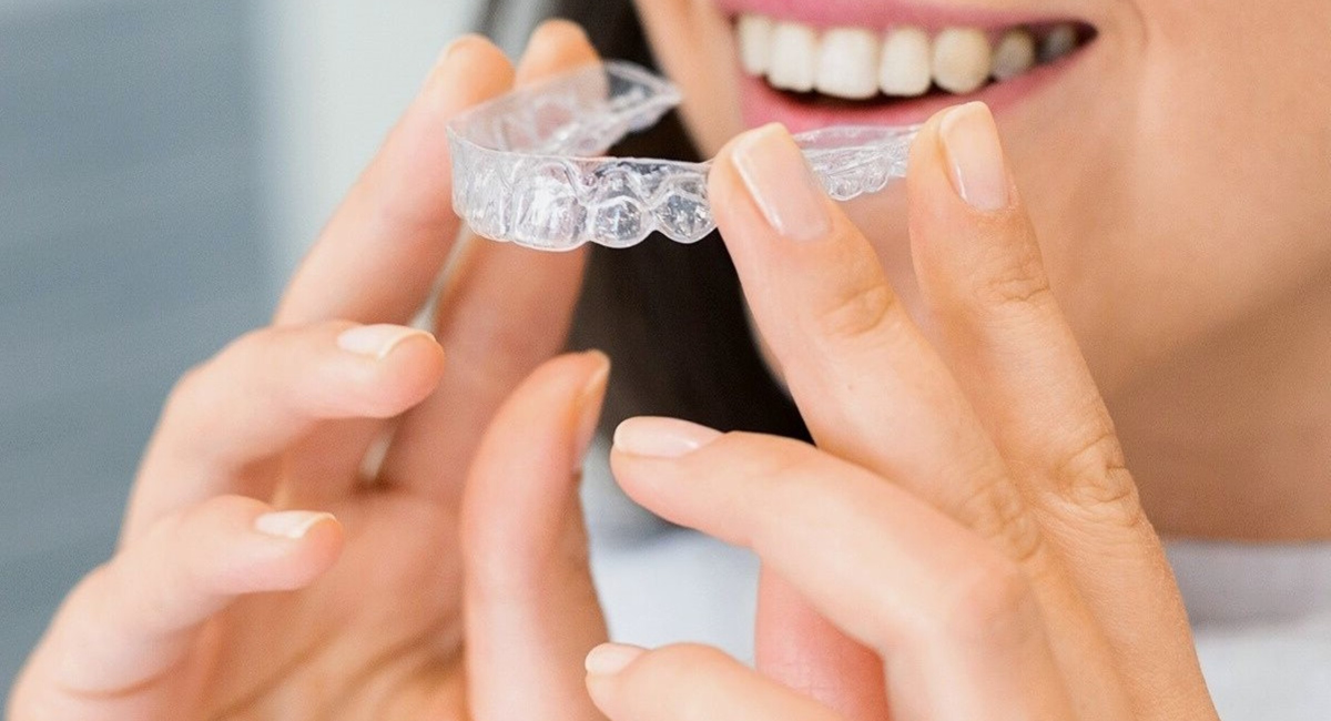A woman is holding a clear brace in front of her teeth.