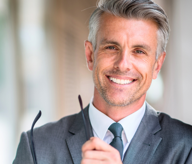 A man in a suit and tie is holding a pair of glasses and smiling.