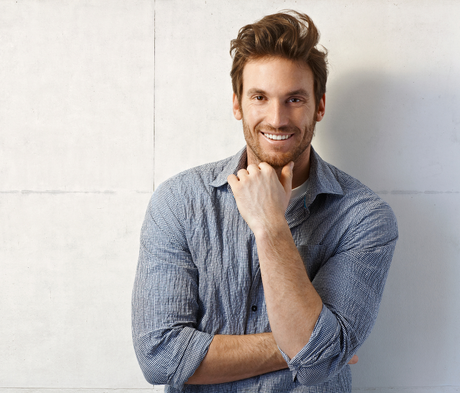 Smiling man with brown hair in a casual button-up shirt, standing against a wall