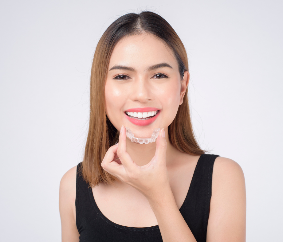 Woman smiling and holding a clear aligner 